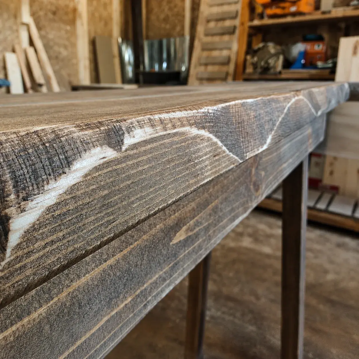 Close-up of a rustic solid wood furniture edge with live-edge movement and visible hand-worked tool marks in the workshop